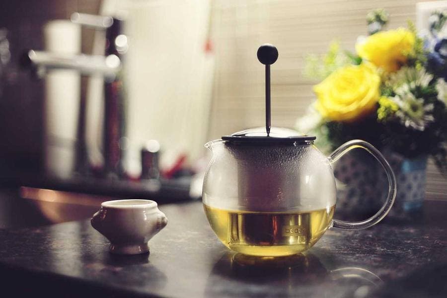 A glass teapot and fresh yellow roses on a kitchen counter